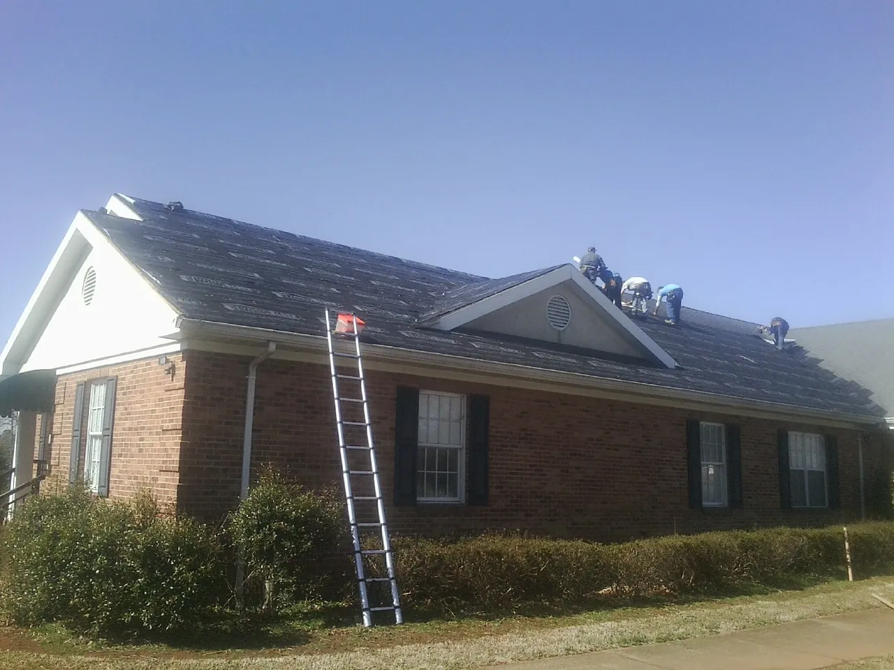 Crew tearing shingles off a brick ranch roof with a ladder set — Metal Roof Repair work by our crew in Dolton
