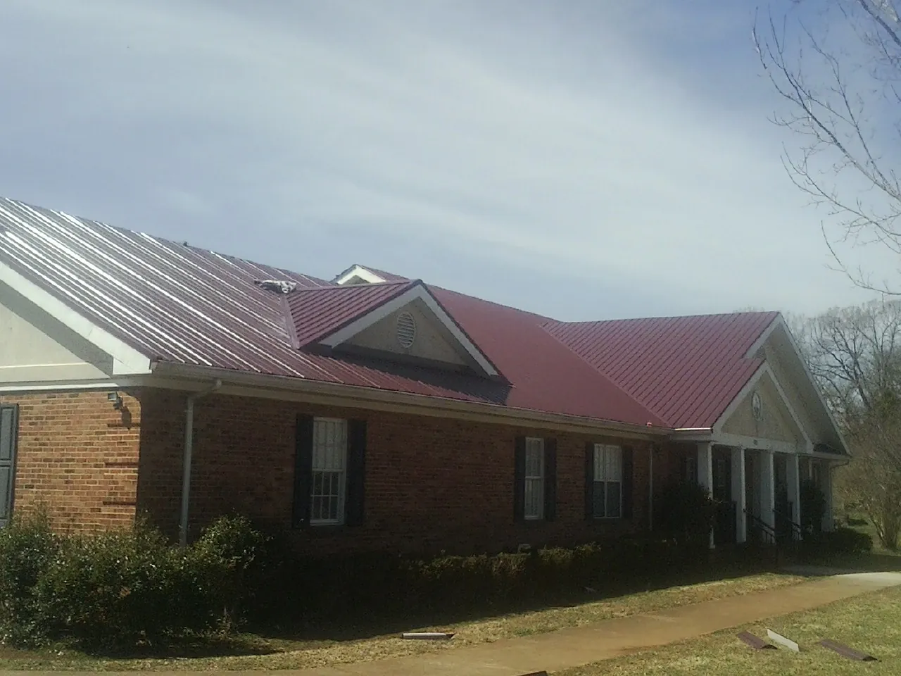 Red metal roof with gabled entries on a long brick building, from a Hail Damage Roof Repair job in Dolton