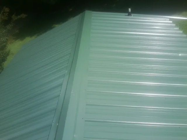 New green metal panels meeting at the ridge of a roof — Flat Roof Repair work by our crew in Dolton