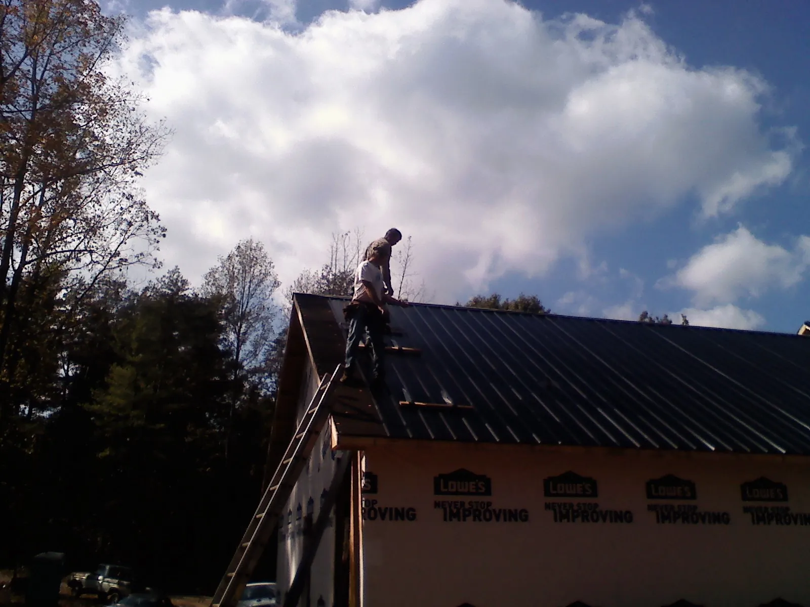 Roofer fastening dark metal panels high against a cloudy sky, from a Roof Inspection job in Dolton